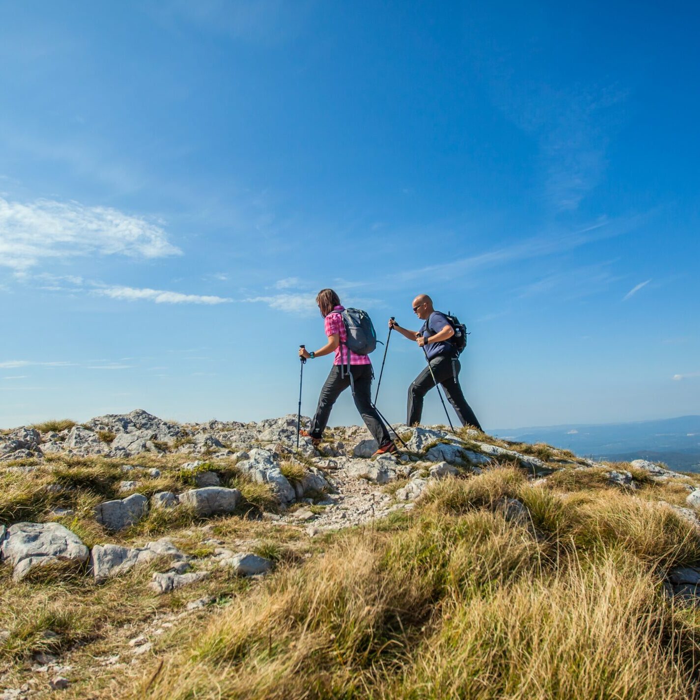 A couple hiking on Nanos Plateau in Slovenia against a blue sky
